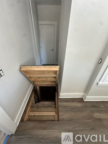 A room with a wooden staircase leading to a hole in the floor.