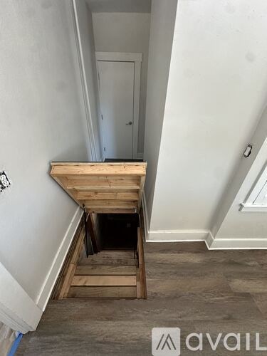 A room with a wooden staircase leading to a hole in the floor.