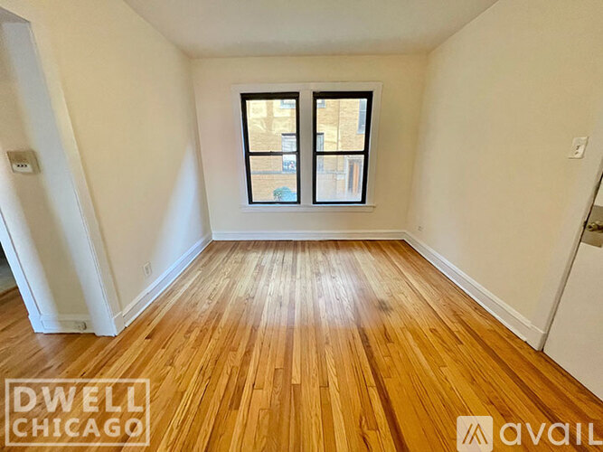 A room with wooden flooring and a window showing a view of a building outside.