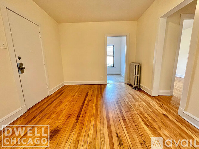 A room with wooden floors and white walls, with a door on the left and a window in the distance.