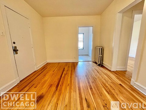 A room with wooden floors and white walls, with a door on the left and a window in the distance.