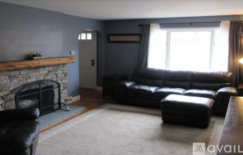 A living room with a black leather couch and a stone fireplace.