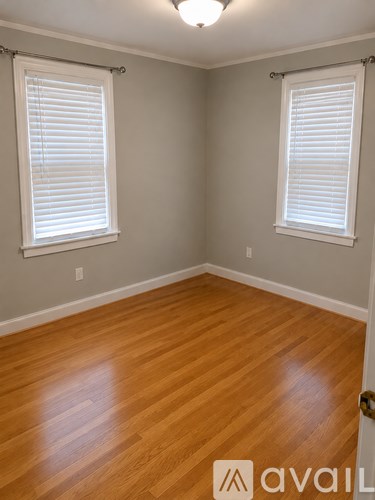A room with wooden floors and two windows with blinds.