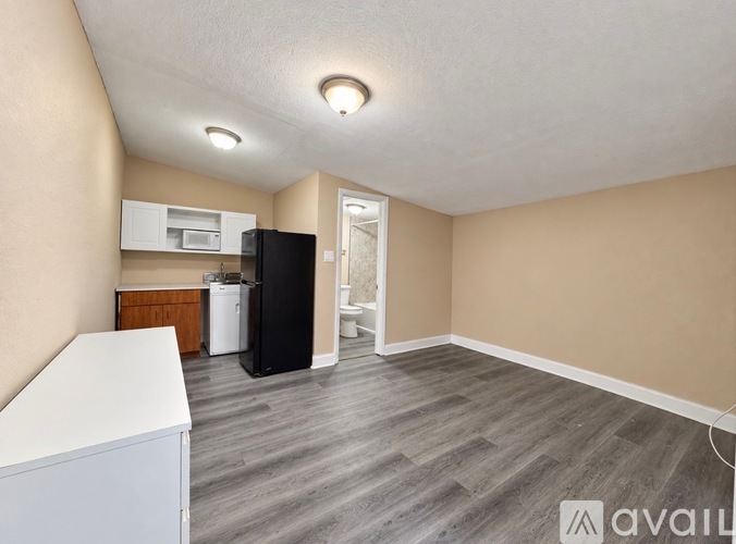 A kitchen with a black fridge, white countertops, and wooden cabinets.