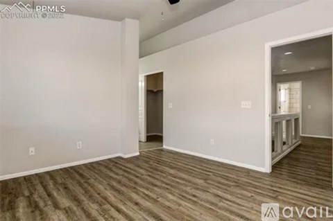 A spacious room with wood flooring and white walls, currently empty and available for rent.