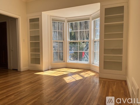 A room with wooden floors and a large window with a view of trees and a red flag.