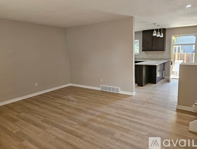 A spacious room with wooden flooring and a kitchen area in the background.