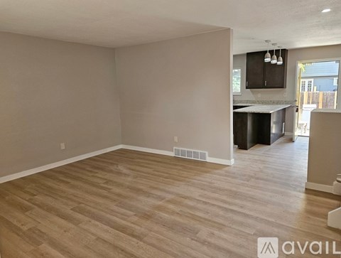 A spacious room with wooden flooring and a kitchen area in the background.