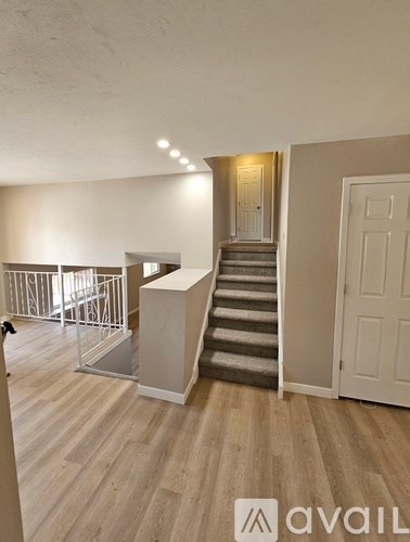 A room with wooden flooring and a staircase leading to another room.