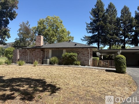 A house with a brown roof and a chimney is surrounded by trees and has a driveway leading to the front door.