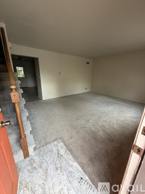 A room with a carpeted floor and a wooden staircase.