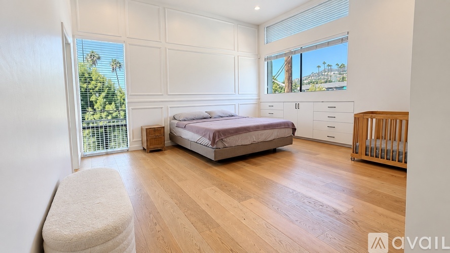A bedroom with a large bed, a window with a view of trees, and a wooden floor.