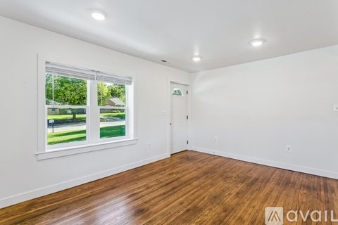 A room with wooden floors and a window showing a green outdoor area.