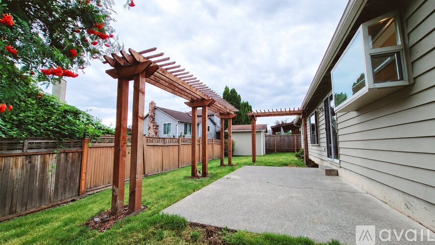 A wooden pergola with red flowers is in front of a house.