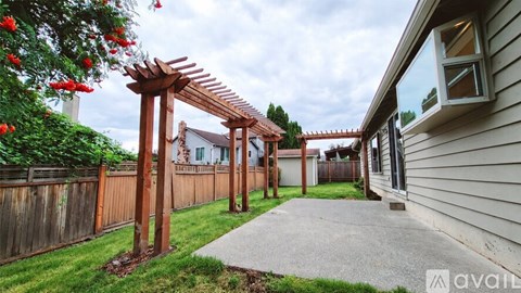 A wooden pergola with red flowers is in front of a house.
