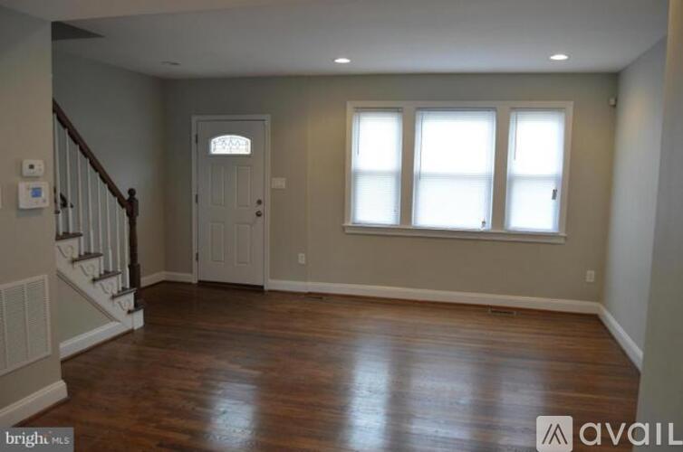 A spacious room with wooden floors and a staircase on the left side.