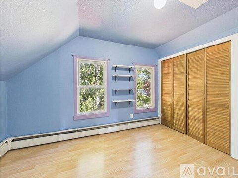 A room with blue walls and wooden flooring, featuring a window with a view of trees and a sliding door.