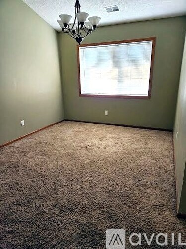 A room with a carpeted floor, a window with blinds, and a chandelier.
