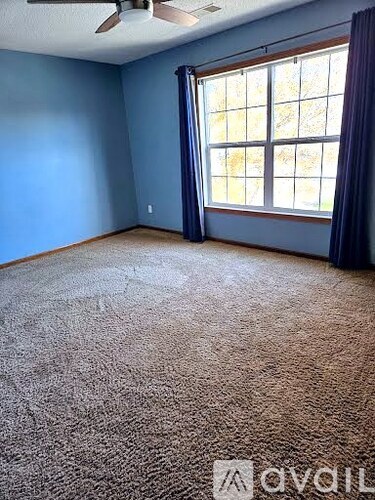 A room with a carpeted floor, a ceiling fan, and a window with blue curtains.