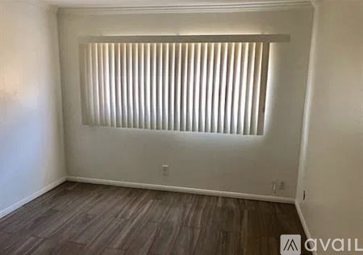 A room with a window covered by white blinds and wooden flooring.