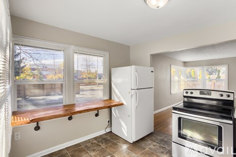 A kitchen with a white refrigerator and stove, a window with blinds, and a window seat.