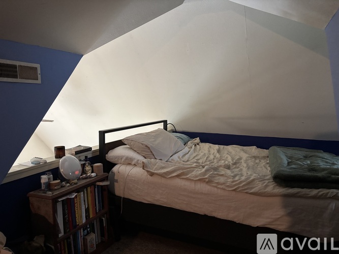 A bedroom with a bed, a nightstand with a lamp, and a bookshelf.