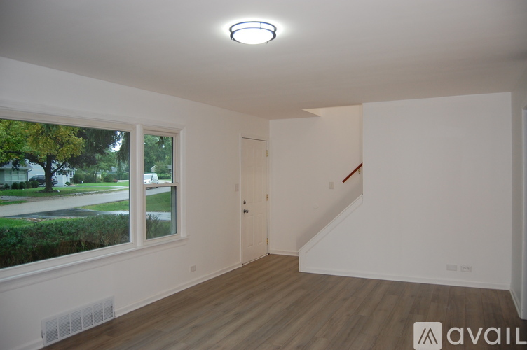A room with a window overlooking a street and a wooden floor.