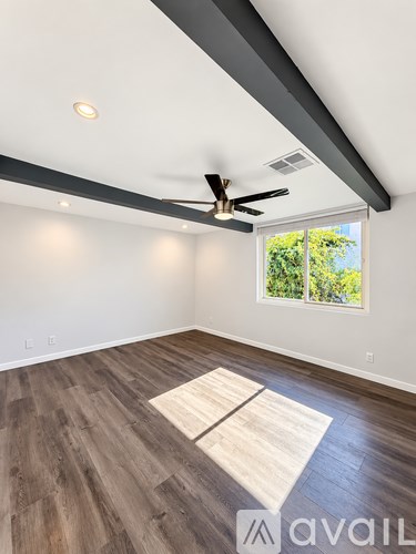 A room with a ceiling fan and a window showing greenery outside.