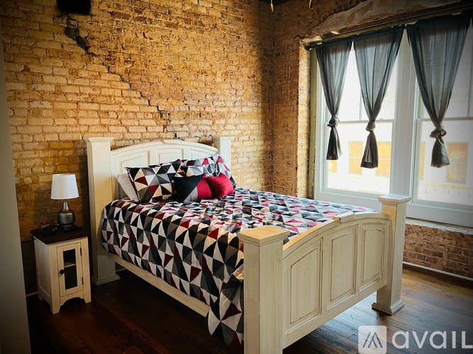 A bed with a white headboard and a black and white quilt sits in a room with a brick wall.