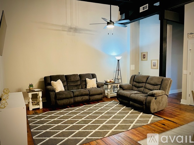 A living room with a grey rug and a black ceiling fan.