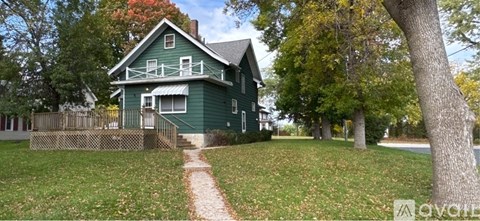 A green house with a wooden fence and a tree in front.