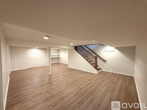 A spacious room with wooden flooring and a staircase.