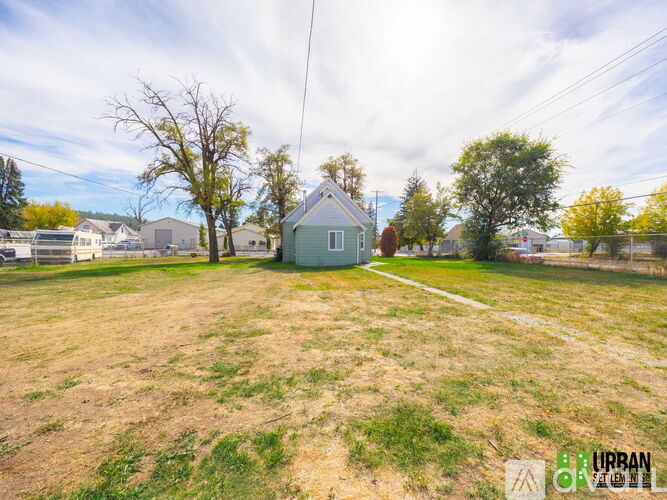 A field with a house and trees in the background.