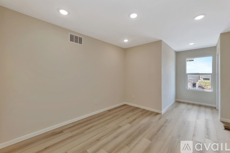 A spacious room with wooden flooring and a window overlooking a building.