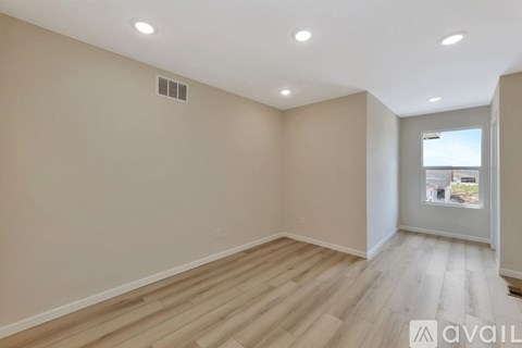 A spacious room with wooden flooring and a window overlooking a building.