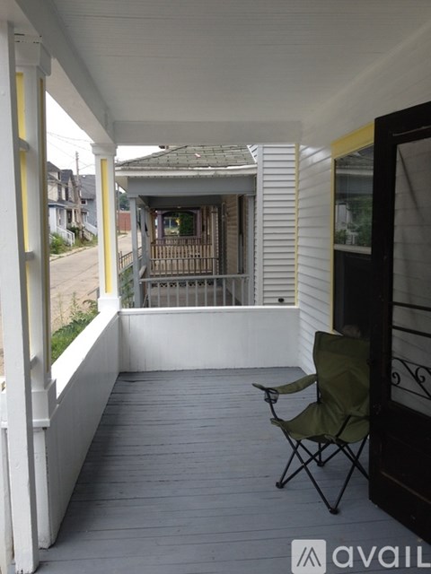 A chair is on a porch with a view of a house and trees.