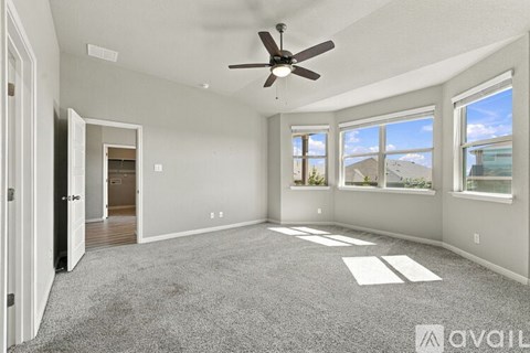 A spacious living room with a ceiling fan and large windows.