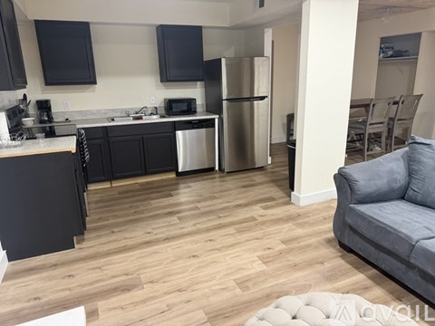 A kitchen with black cabinets and a grey couch.