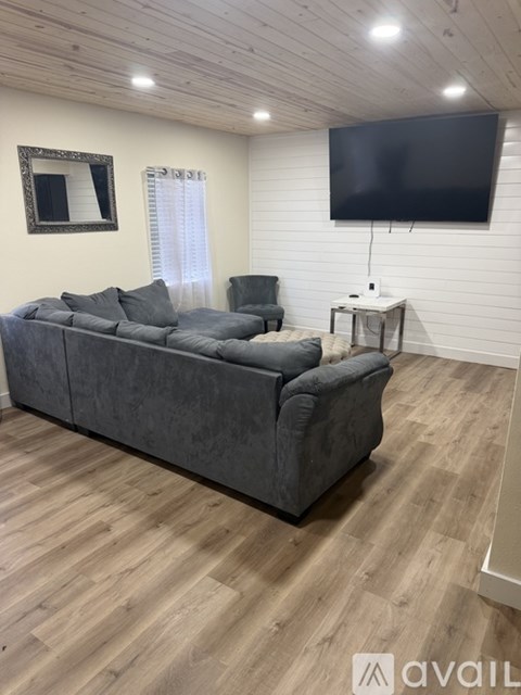 A grey couch sits in a room with wooden flooring and a flat screen TV mounted on the wall.