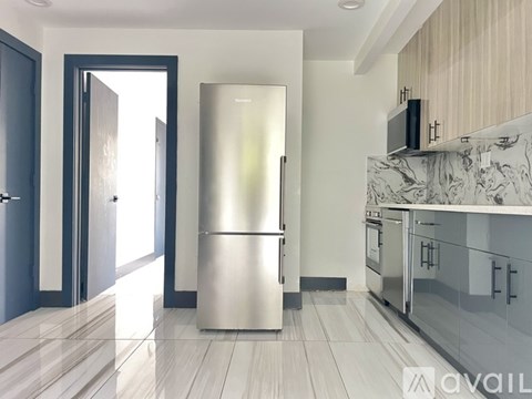 A modern kitchen with a stainless steel refrigerator and wooden flooring.