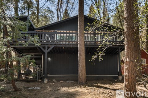 A black house with a balcony surrounded by trees.