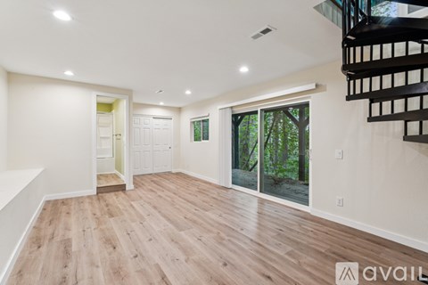 A spacious room with wooden flooring and a staircase on the right side.