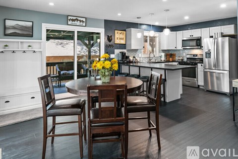 A kitchen with a table and chairs in the foreground and a fridge with a sign on it in the background.