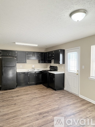 A kitchen with black appliances and cabinets in a room with wooden flooring.