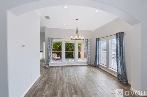 A spacious room with a chandelier and a view of a patio through the sliding glass doors.