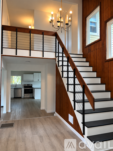 A staircase with a black railing and white steps leads to a kitchen.