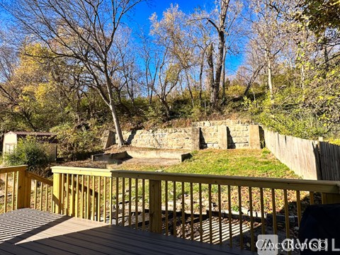 A wooden deck overlooks a grassy area with trees and a stone wall.