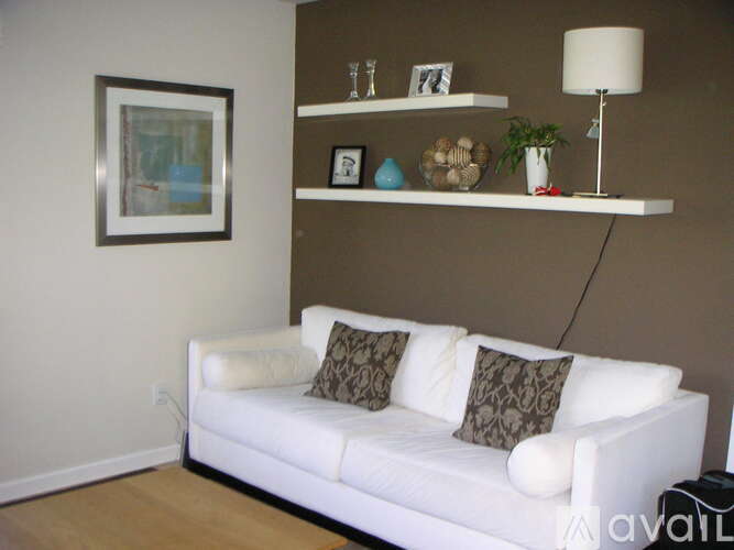 A white couch with two brown pillows sits in front of a wall with a framed picture and a shelf with various decorative items.
