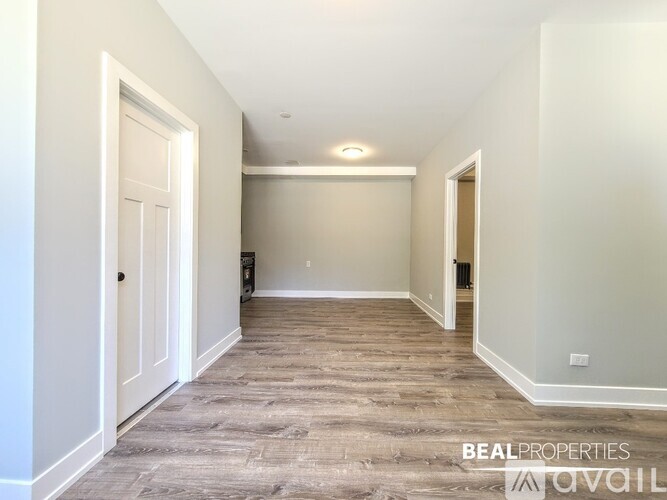 A spacious room with wood flooring and white walls, with a door on the left and a window on the right.
