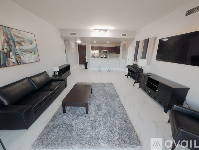 A living room with a black leather couch and a grey rug.